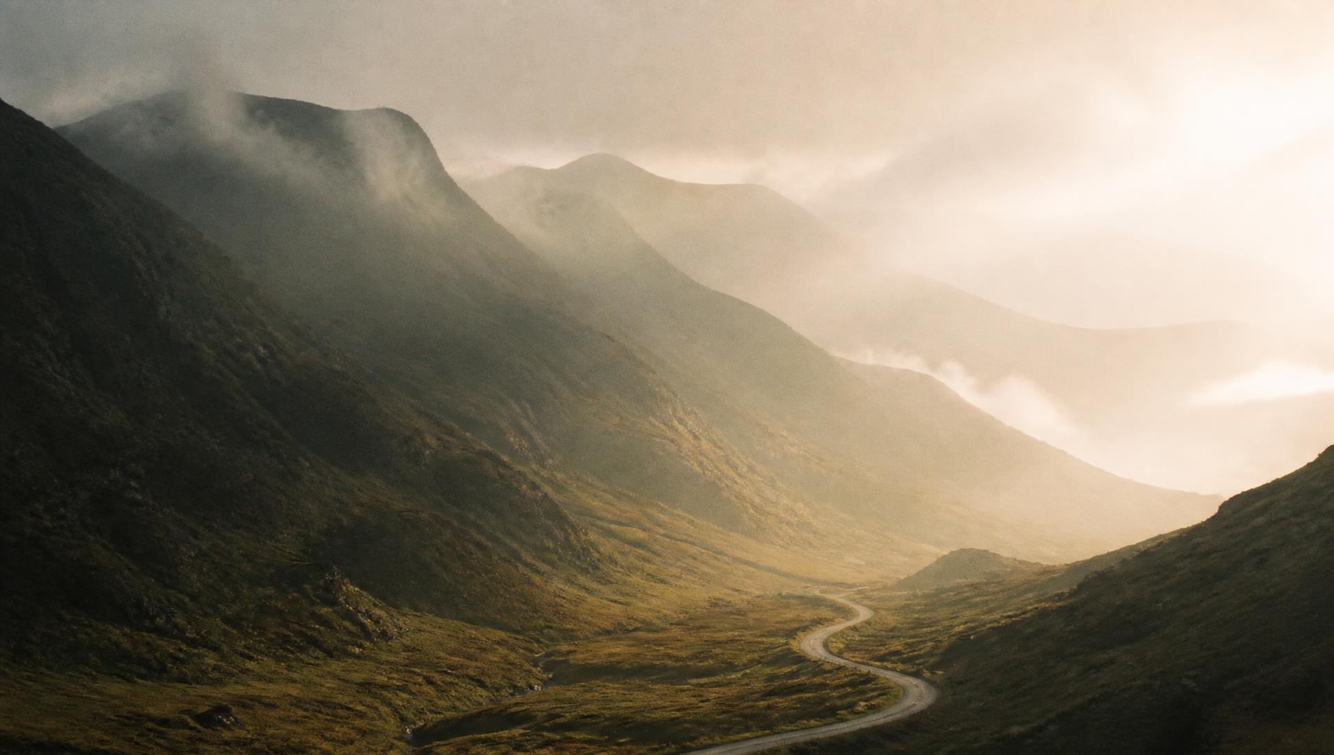 A misty mountain valley at first light with a single winding road